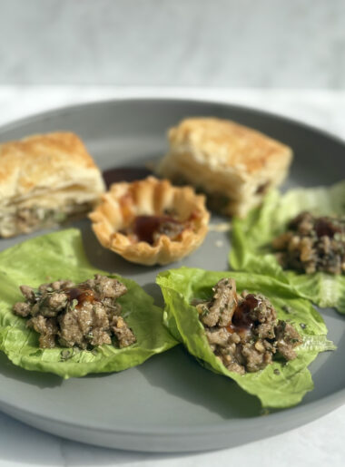 A plate contains three lettuce cups filled with turkey, cashew, and mushrooms; in the background, the same filling is presented in puff pastry and pastry shells