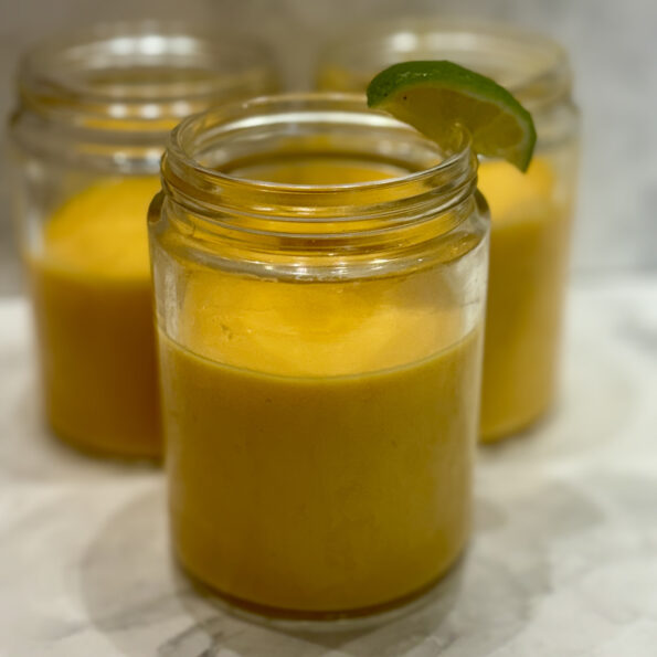 Three mason jars are filled with a carrot mango smoothie.