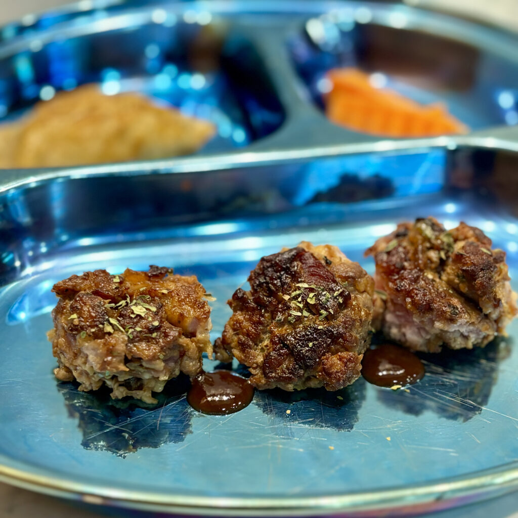 A trio of Vietnamese style pork meatballs are plated with some dollops of barbecue sauce.