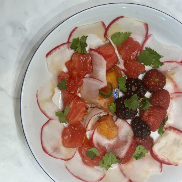 A plate is filled with a kid-friendly salad: radishes encircle, with tomatoes, berries, and oranges inside.