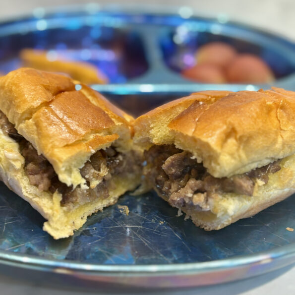 A chopped cheese sandwich is split in half and displayed so that the meat and cheese is visible inside the hoagie roll.