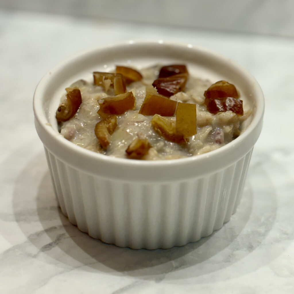 A ramekin holds a creamy banana porridge, its top studded with chopped dates.