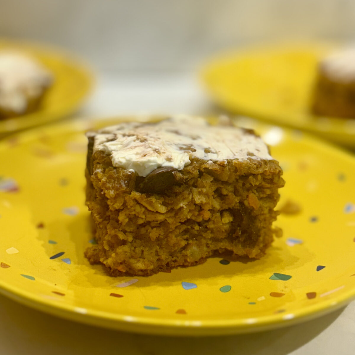 A slice of a carrot, cashew, and oat bar is presented to show its chocolate inside and icing on top.