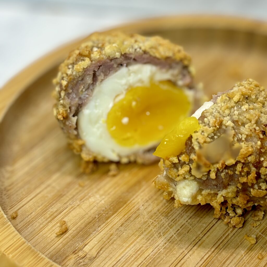 Closeup on a halved scotch egg, with interior yolk and whites visible, as well as the surrounding pork and breadcrumb crust.