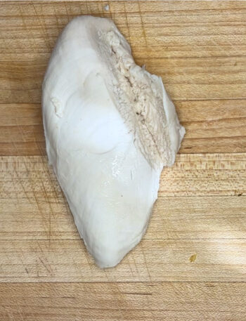 A cooked chicken breast sits on a cutting board, awaiting slicing.