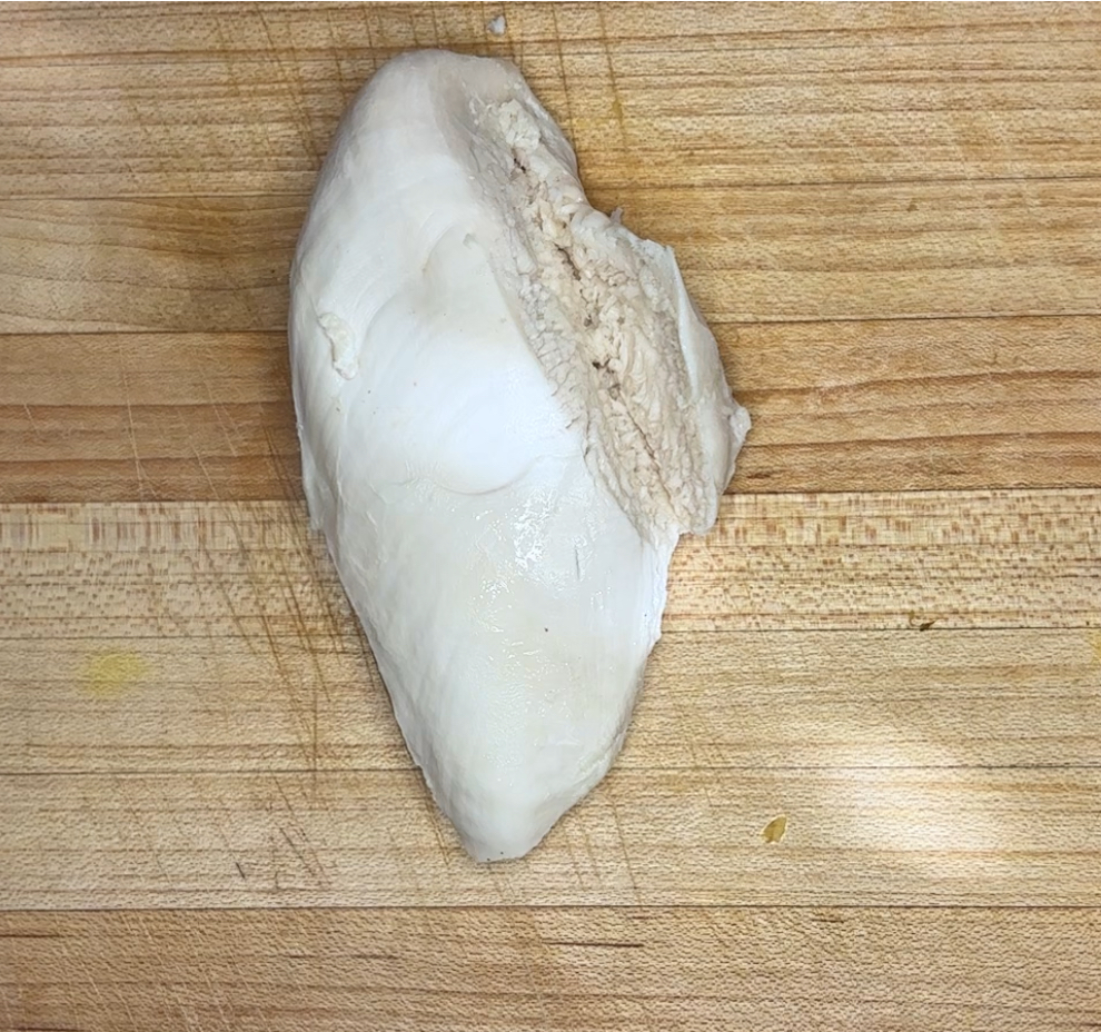 A cooked chicken breast sits on a cutting board, awaiting slicing.