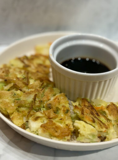 Slices of a fried vegetable pancake surround a small ramekin of soy sauce.