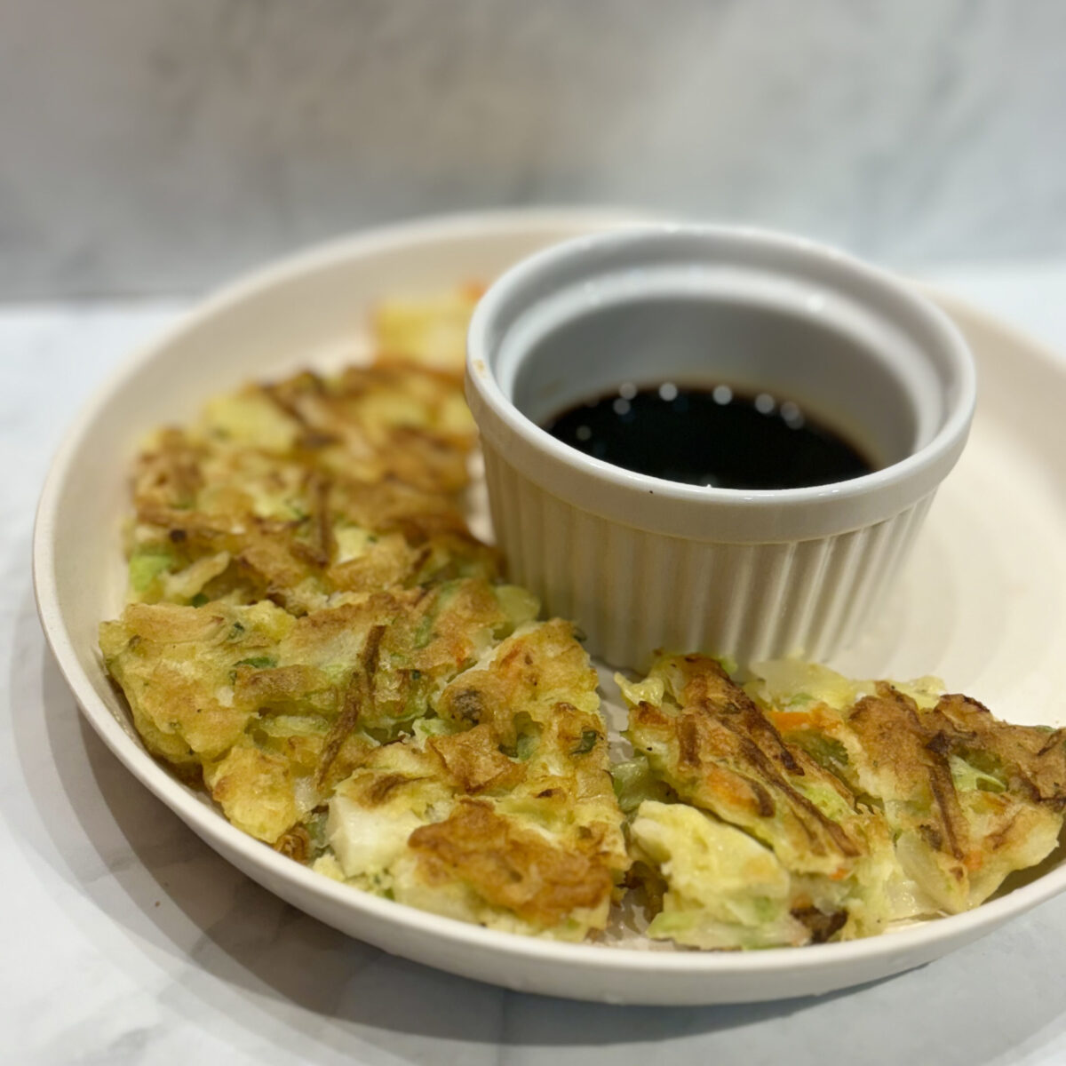 Slices of a fried vegetable pancake surround a small ramekin of soy sauce.