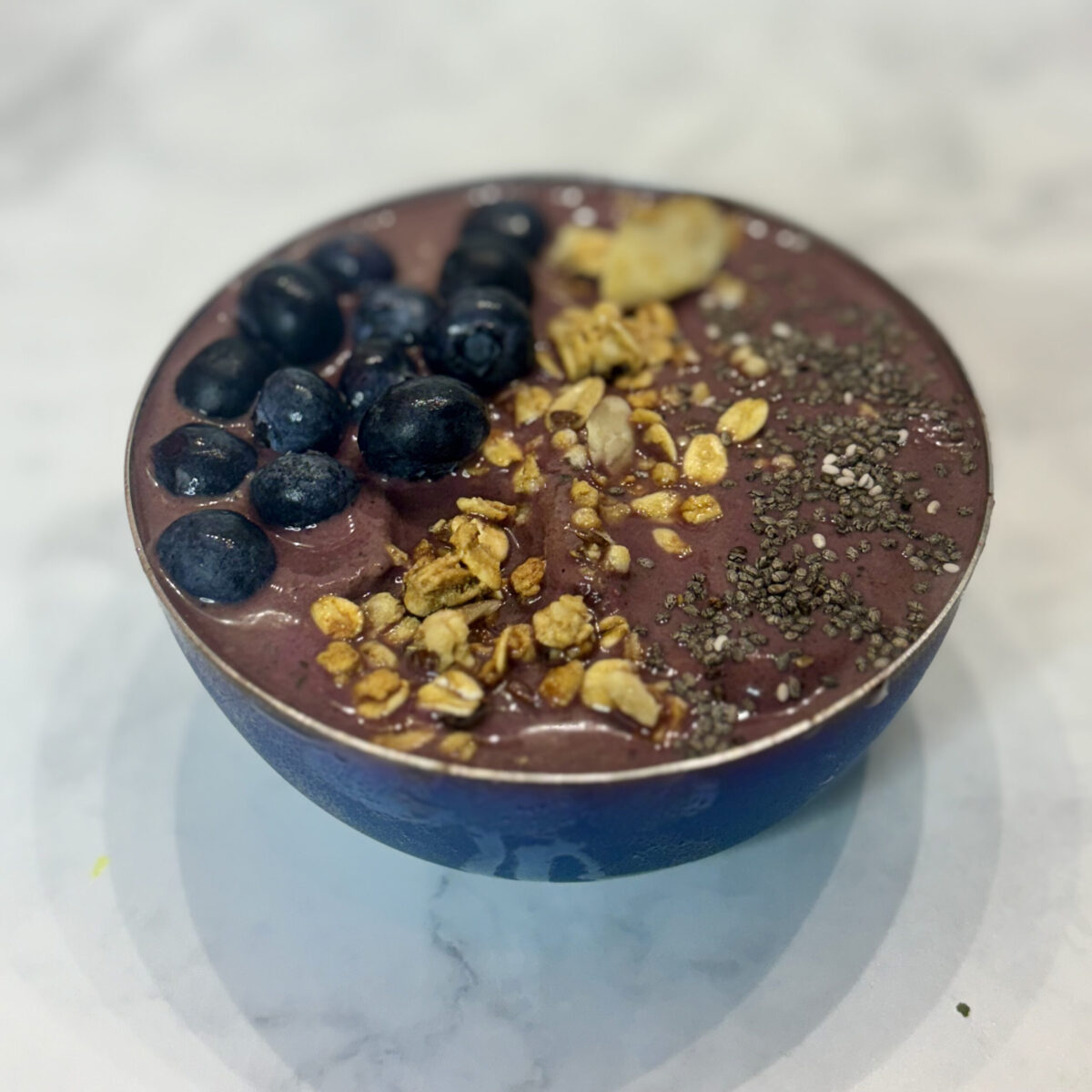 A smoothie bowl filled with acai, spinach, and cottage cheese is topped with granola, blueberries, and chia seeds