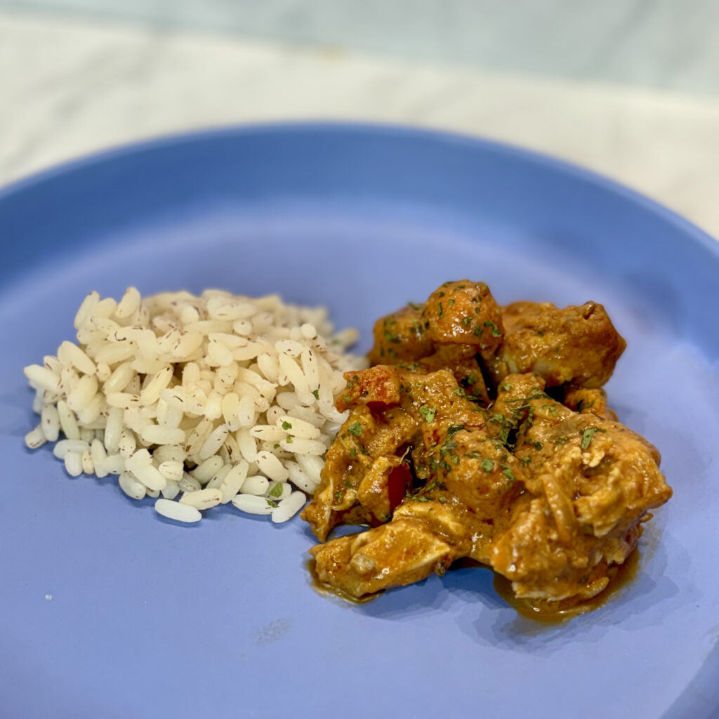 A plate holds a pile of peanut butter stew, with pieces of chicken, carrot, and sweet potato visible; it is sided by a mound of rice.