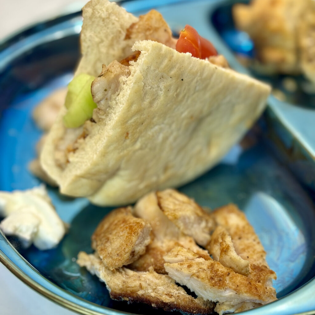 A plate holds pieces of toddler shawarma, as well as a small pita sandwich containing shawarma pieces, tomato, and cucumber.