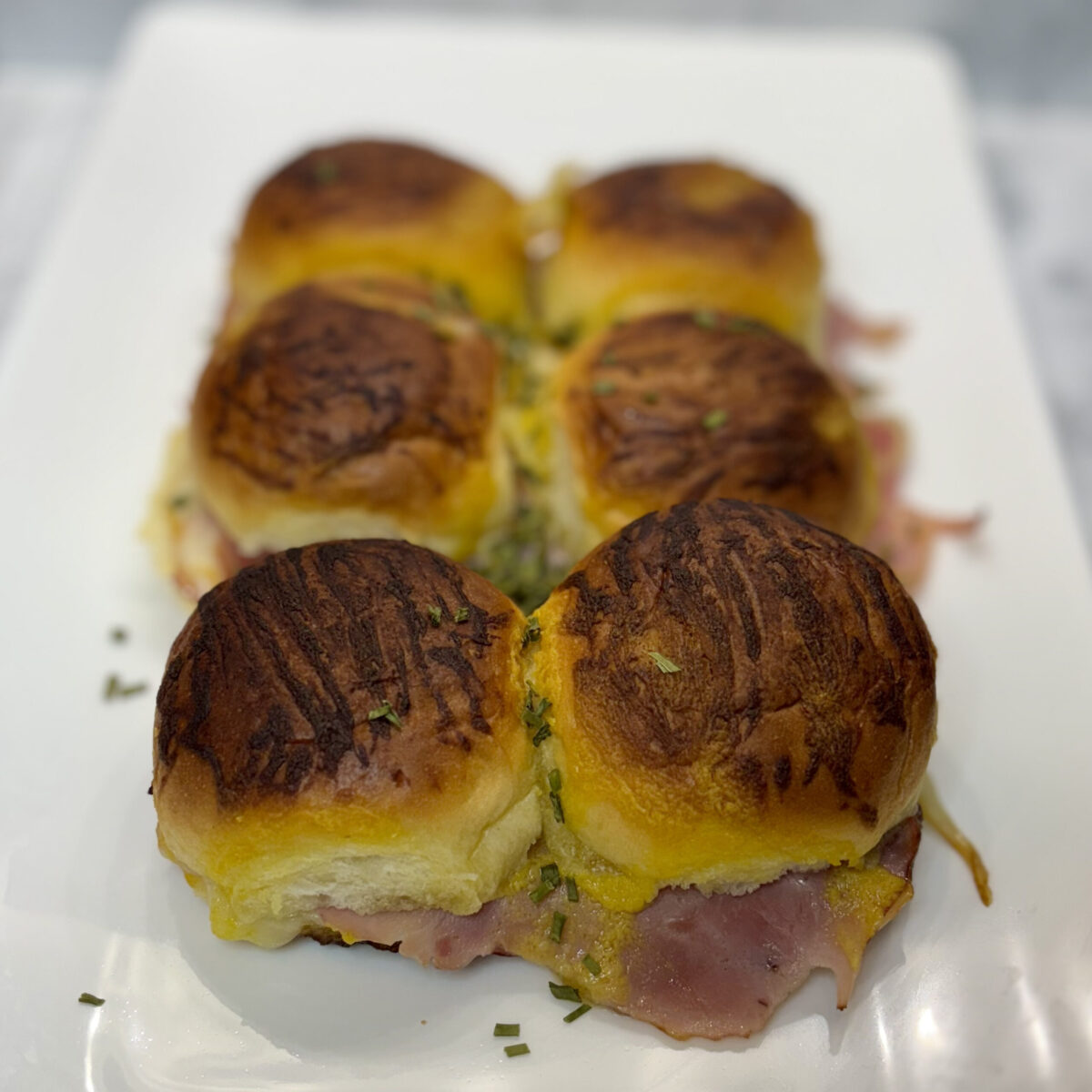 A set of six ham and cheese sliders are displayed on a plate, the meat and melted cheese visible in the foreground.