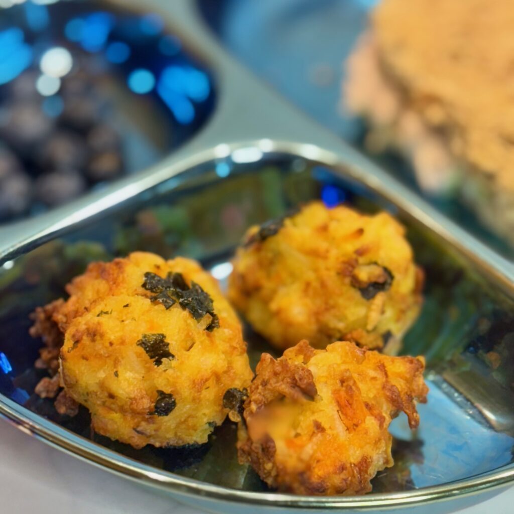 A trio of carrot-rice balls (i.e., toddler arancini) front a plate that also includes a sandwich and blueberries.