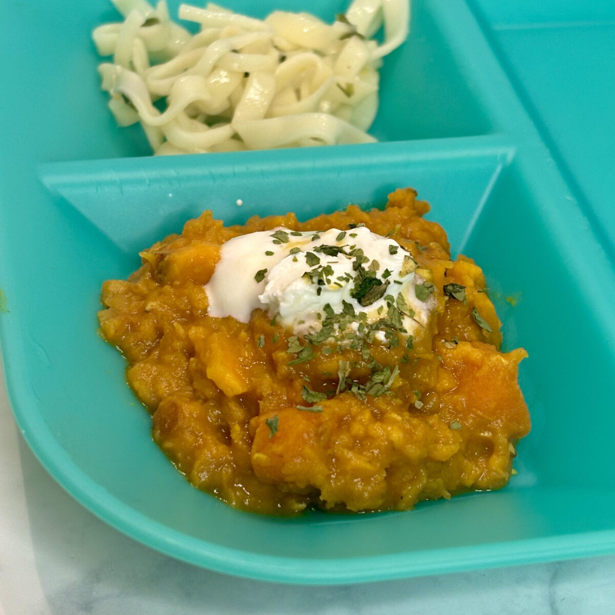 Lentils for infants served in the compartment of a toddler meal plate; yogurt is on top.