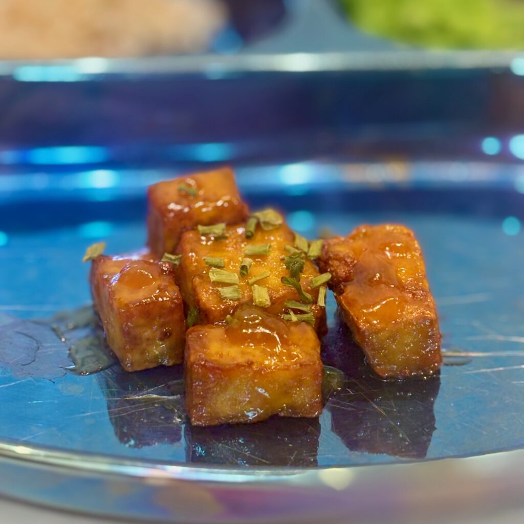 Cubes of toddler orange chicken are covered in orange sauce and adjacent on a plate.