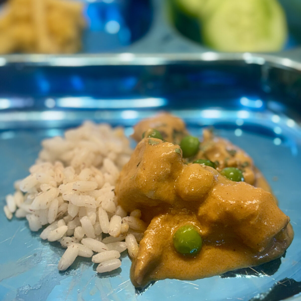 A toddler butter chicken, studded with peas, is sided with ricec.