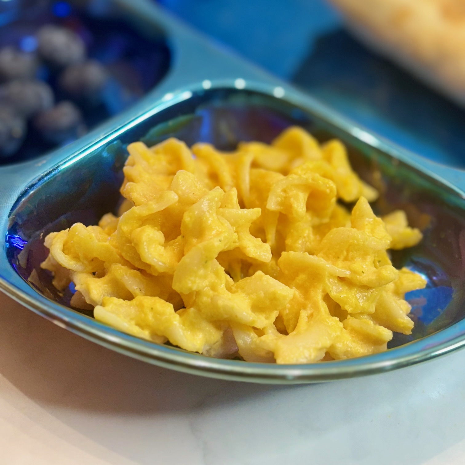 A side of macaroni and cheese, its sauce containing vegetables, is presented on a dinner plate.