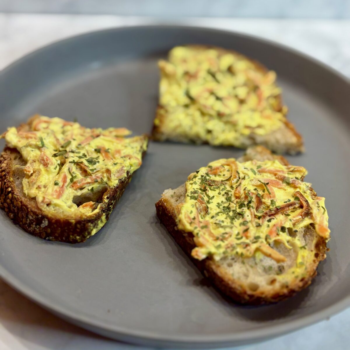 Slices of toast topped with a carrot and yogurt dip are shown on a plate.