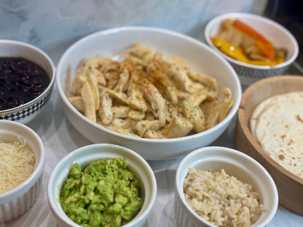 All ingredients and toppings for fajitas for kids on display: chicken, peppers, tortillas, guacamole, beans, etc.