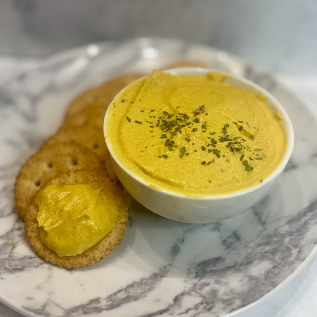 A bowl of carrot dip is sided with crackers for spreading.