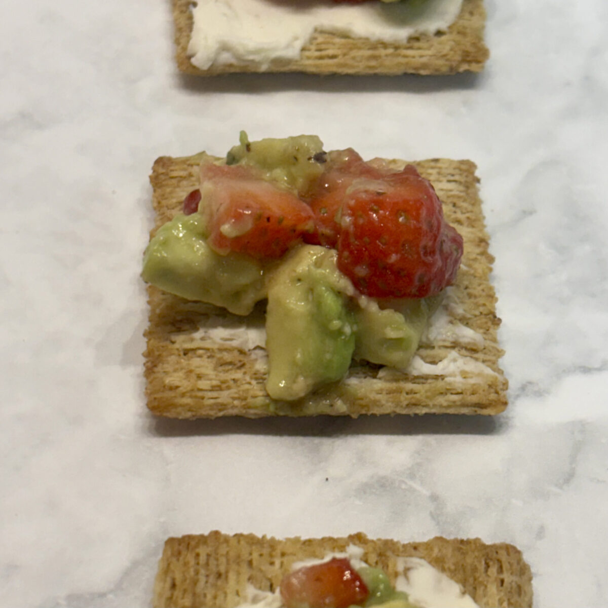 Toddler avocado snack of strawberries, avocado, and cream cheese on top of a cracker.