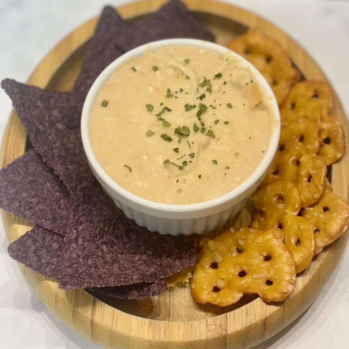 Queso dip for kids, shown presented in a ramekin and sided by tortilla chips and pretzel crackers.