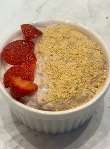 A ramekin of strawberry cheesecake overnight oats for toddlers is shown topped with graham cracker crumbs and diced strawberries.