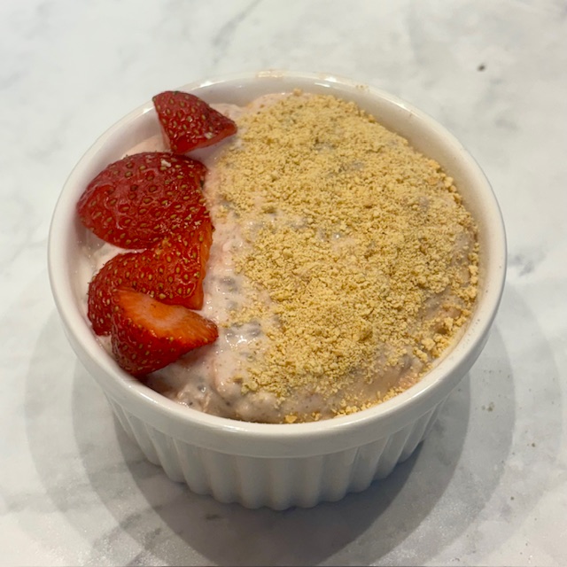 A ramekin of strawberry cheesecake overnight oats for toddlers is shown topped with graham cracker crumbs and diced strawberries.