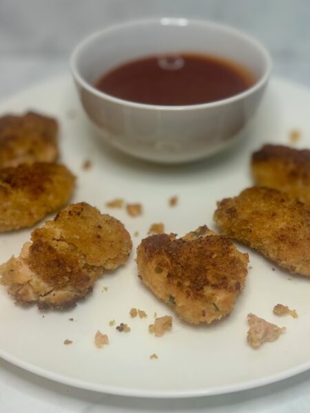 Fingers of the best toddler salmon cakes line a plate; a ramekin of ketchup sidles up next to them.