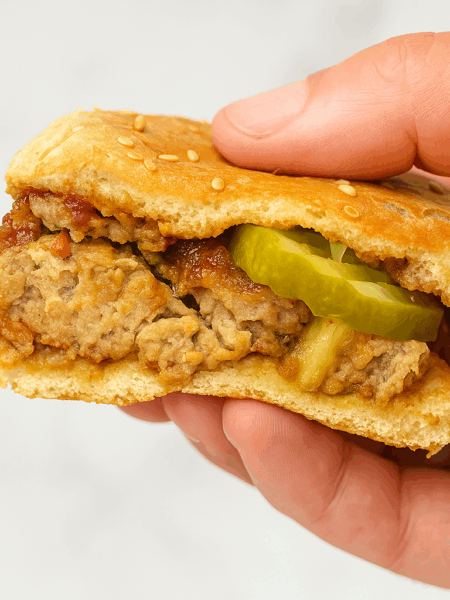 Half of a toddler meatloaf sandwich is held up to show its cruster, interior, and a pickle for some added zing.