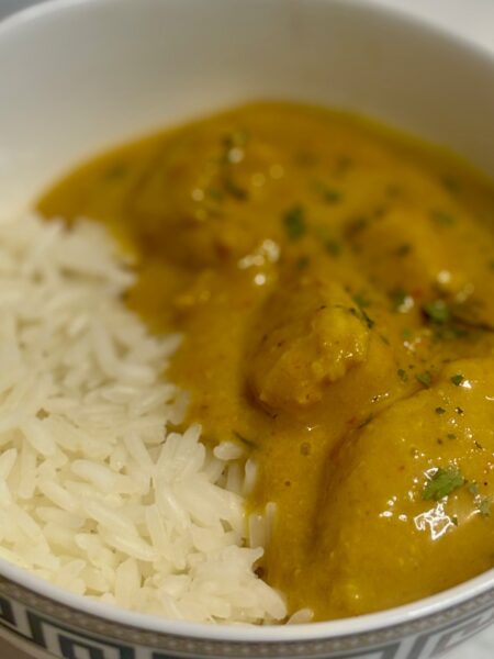 A toddler chicken curry, flavored with mango, is plated next to a heaping pile of coconut rice.