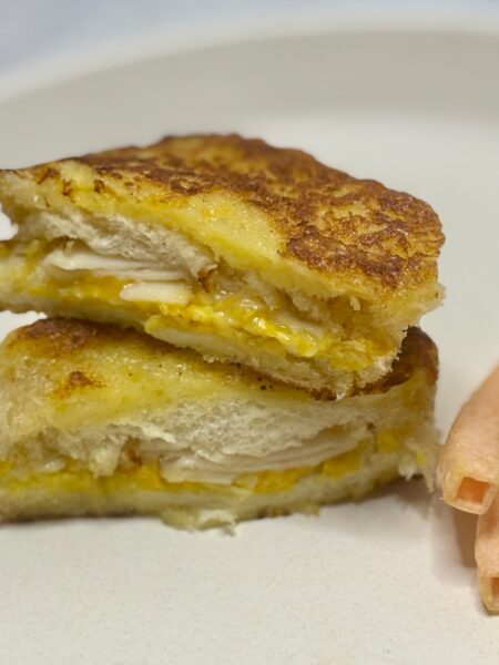 Two halves of a monte cristo sandwich for toddlers, with turkey, cheddar, and a custard crust exposed.