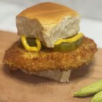 A breaded pork tenderloin fit for a toddler is presented on a hawaiian roll and dressed with mustard and pickles
