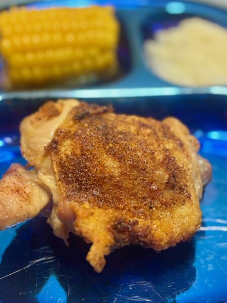 A piece of barbecue chicken for toddlers is shown in the foreground, with crispy, spice-rubbed skin.