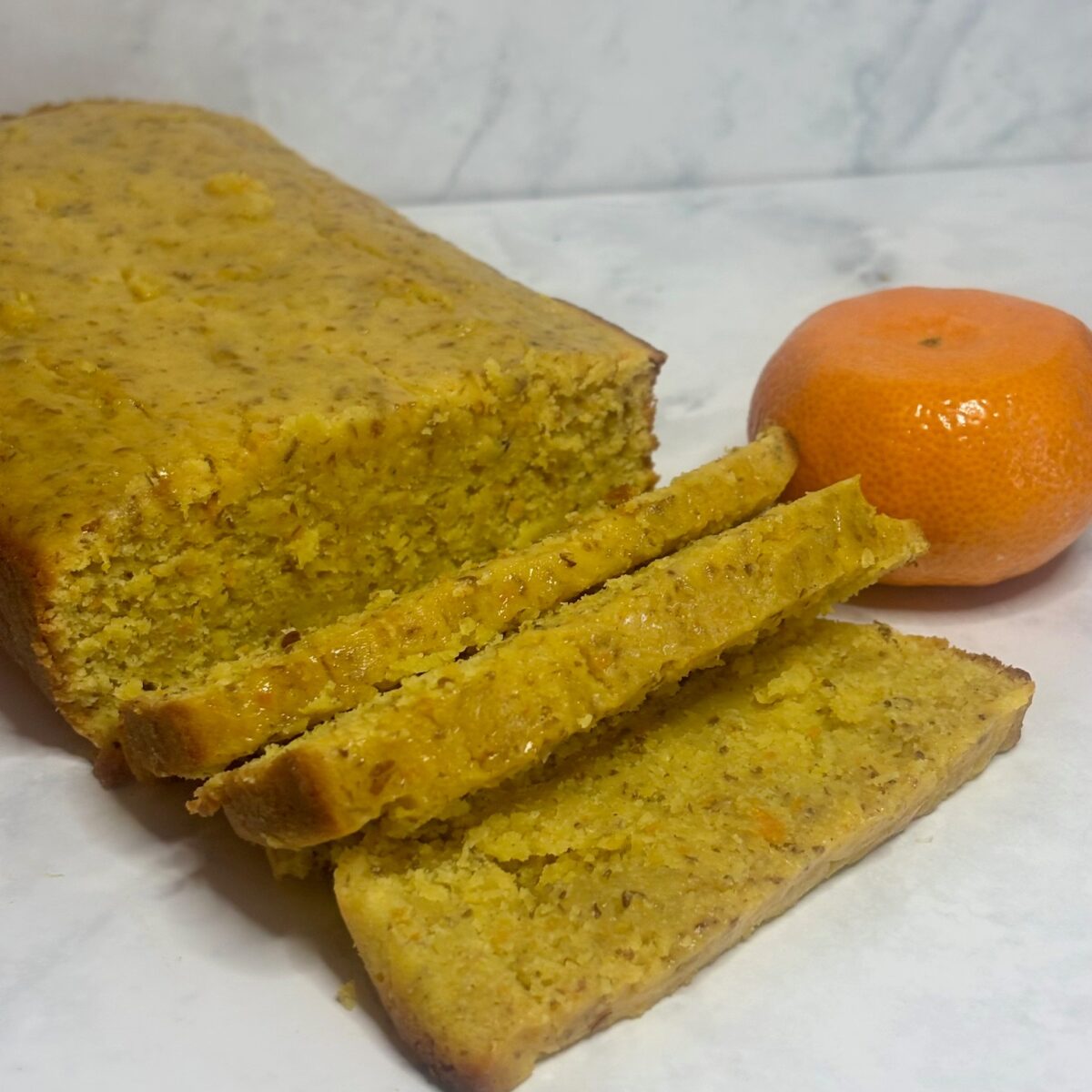 A cake made from leftover clementines is shown in loaf form, with some slices cut.