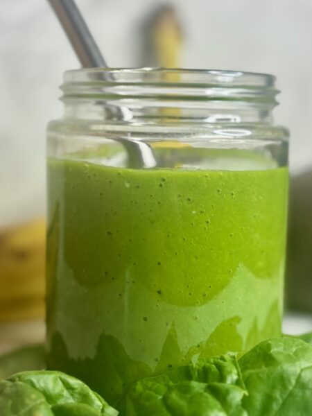 Kids green smoothie recipe shown, surrounded by ingredients: spinach, avocado, banana.