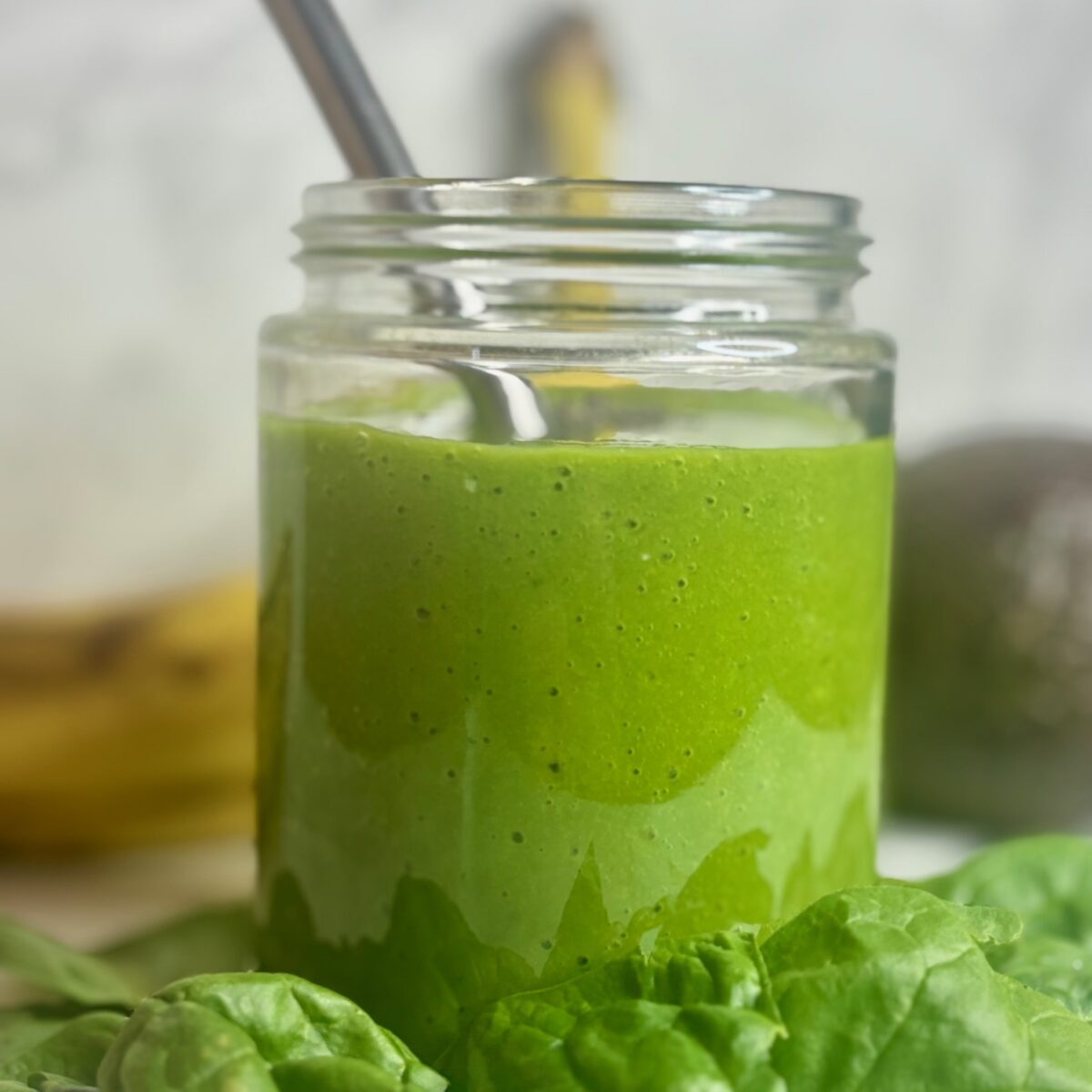Kids green smoothie recipe shown, surrounded by ingredients: spinach, avocado, banana.