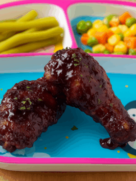 Toddler friendly chicken wings are displayed--they're coated in a blackberry and garlic sauce and plated with vegetables.