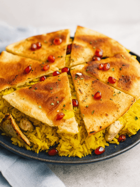 A Persian chicken rice is shown, topped with pomegranates and a crispy pita tahdig.