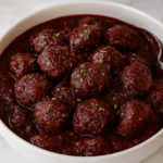 A dozen meatballs swim in a savory cherry sauce.
