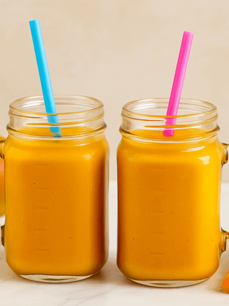 Two cups of toddler mango lassi smoothies are shown next to one another, straws hanging out.