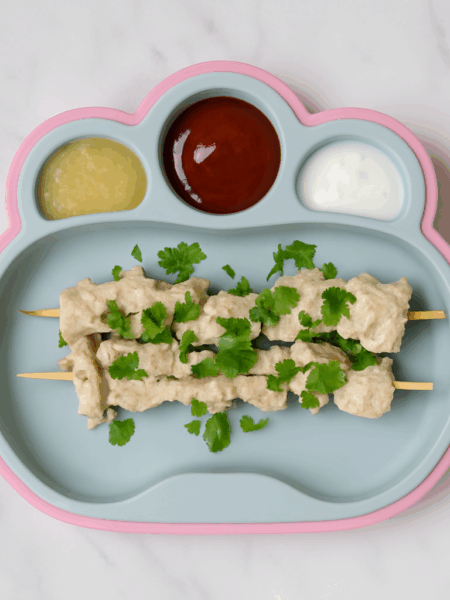 Skewers of chicken kabobs for infants and toddlers line a place, with sauces on the side.