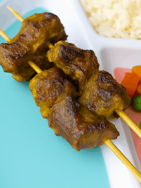 Beef kabobs for toddlers, presented on the skewer and sided by rice and vegetables