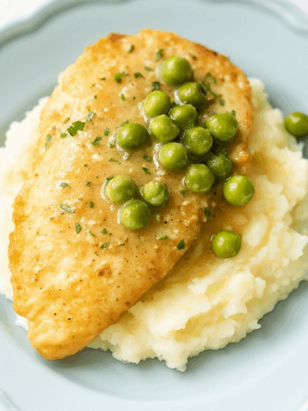 Chicken piccata for kids, showing a breaded chicken breast over mashed potatoes, topped with a pan butter sauce and peas.