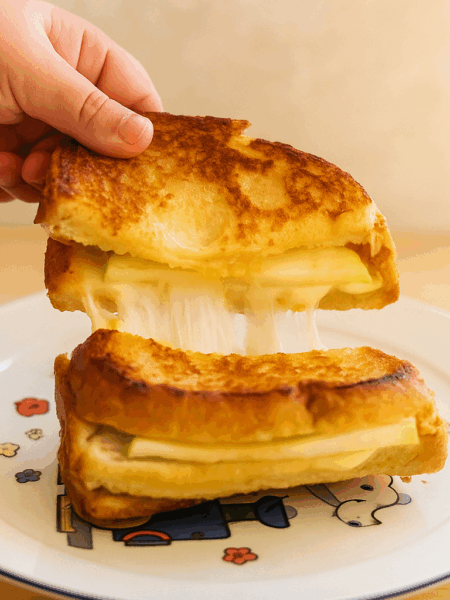 Cheese pull shown on a grilled cheese sandwich stuffed with apples.
