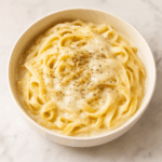 cauliflower fettucine alfredo, topped with cheese and herbs, is shown in a pasta bowl.