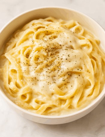 cauliflower fettucine alfredo, topped with cheese and herbs, is shown in a pasta bowl.