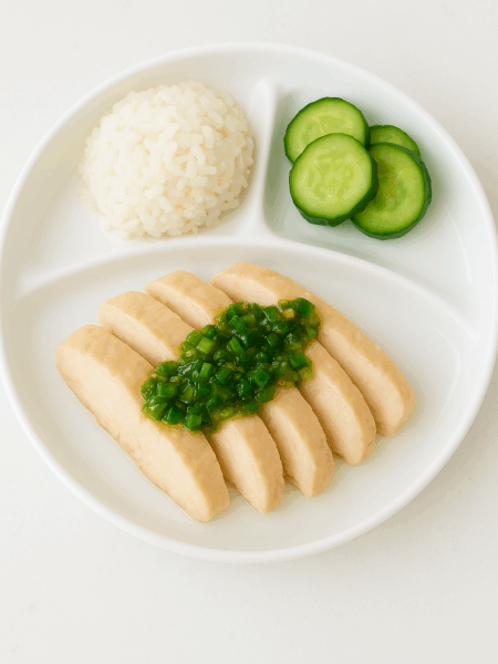 A plate of ginger scallion chicken rice (AKA, Hainan chicken) for toddlers: slices of chicken meat are fanned out in the main compartment, with ginger-scallion oil draped over the top; a mound of rice and cucumbers side the plate.
