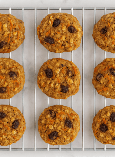 Rows of carrot oatmeal cookies for toddlers are shown resting on a cooling rack, with raisins, carrot strands, and nuts visible.