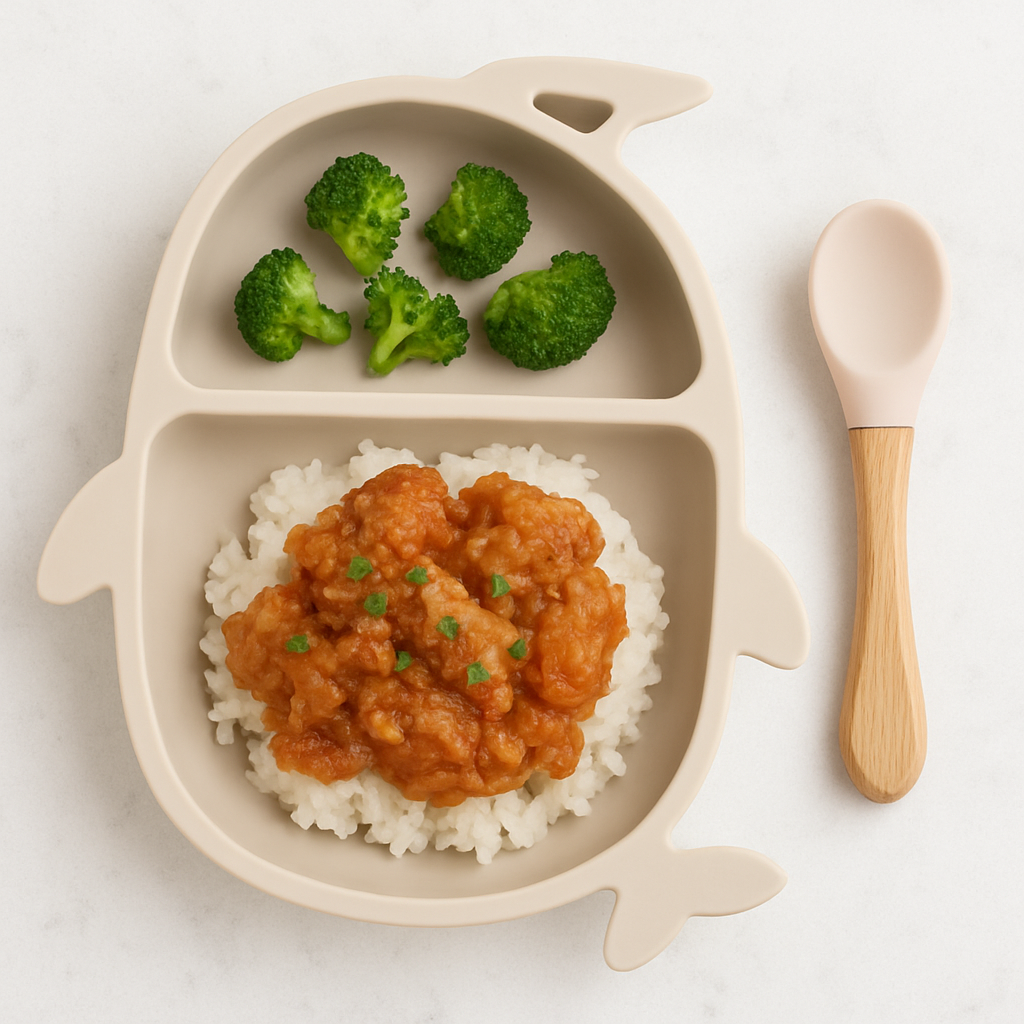 A two-compartment plate shows pieces of saucy cashew chicken strewn atop rice, while above it are several small broccoli florets.